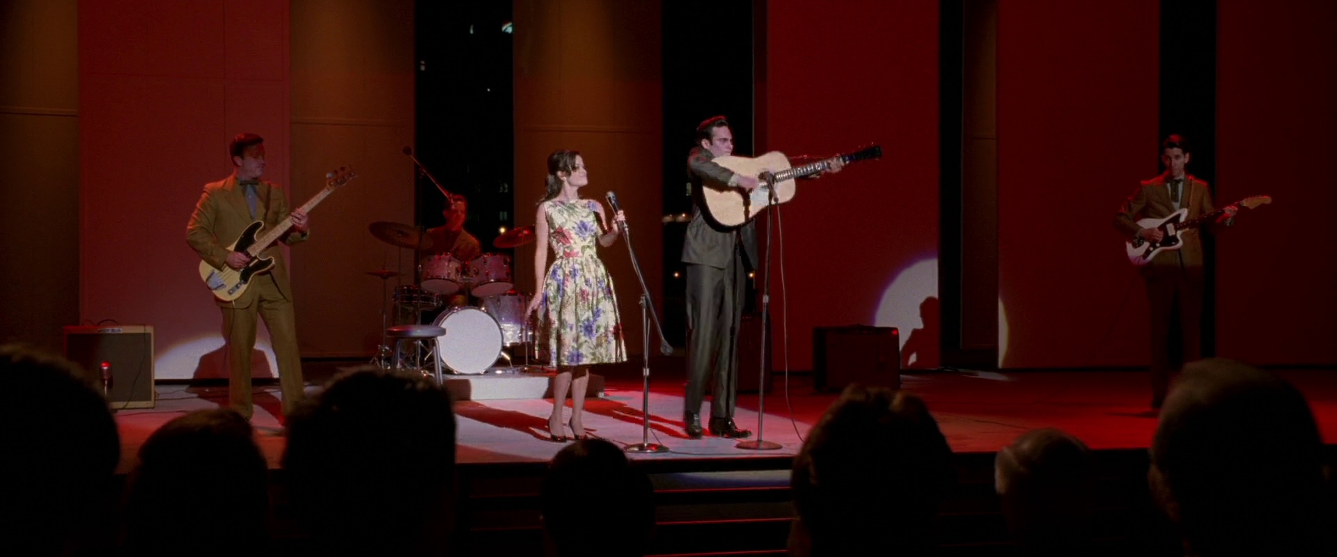 What Is a Biopic? Definition & Film Examples 5 Joaquin Phoenix as Johnny Cash and Reese Witherspoon as June Carter perform on stage with a band under red lighting.