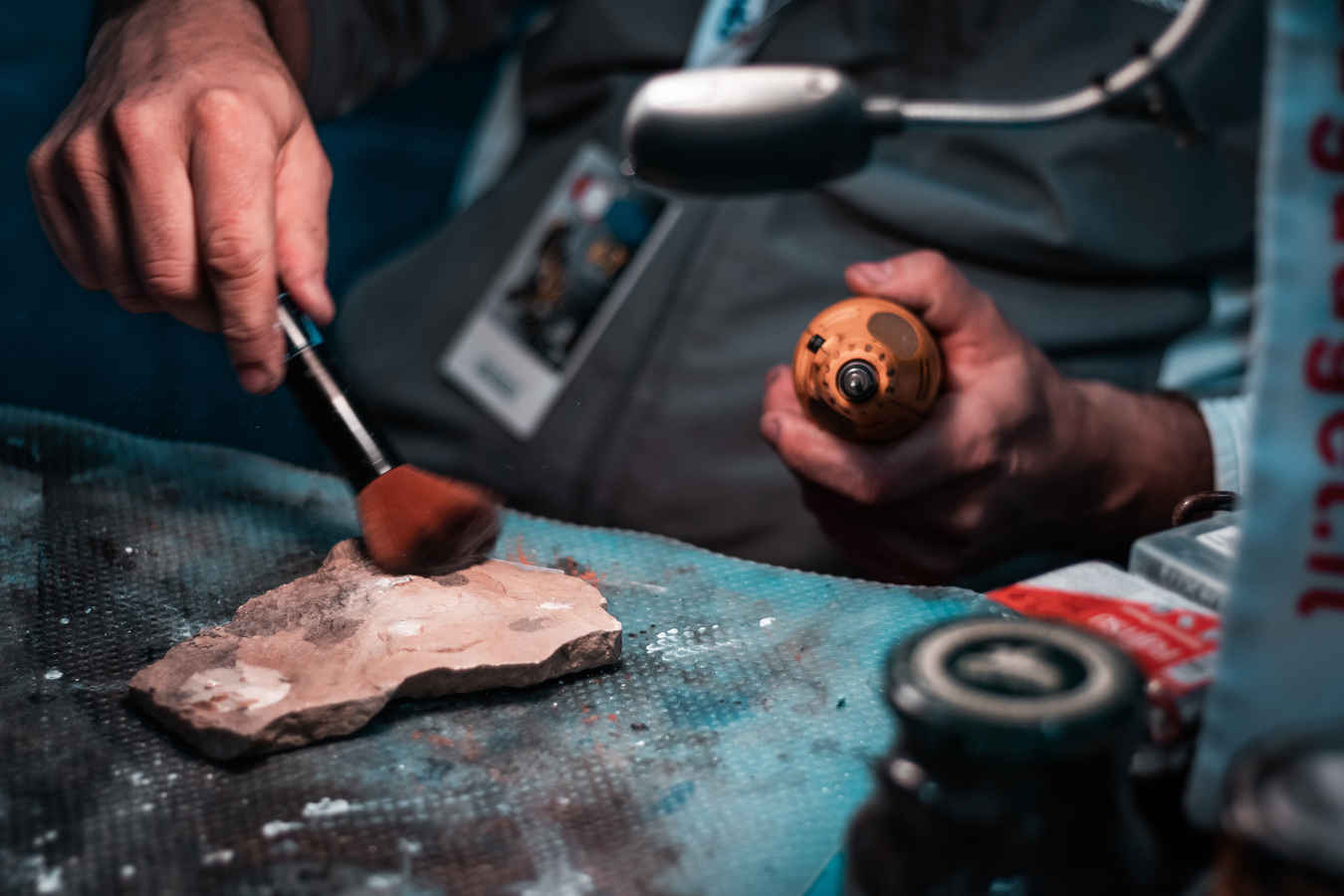 What Is a Scenic Artist? Job Description & Definition 2 Hands of a prop maker using a brush and drill to shape and texture a rock piece for set design.