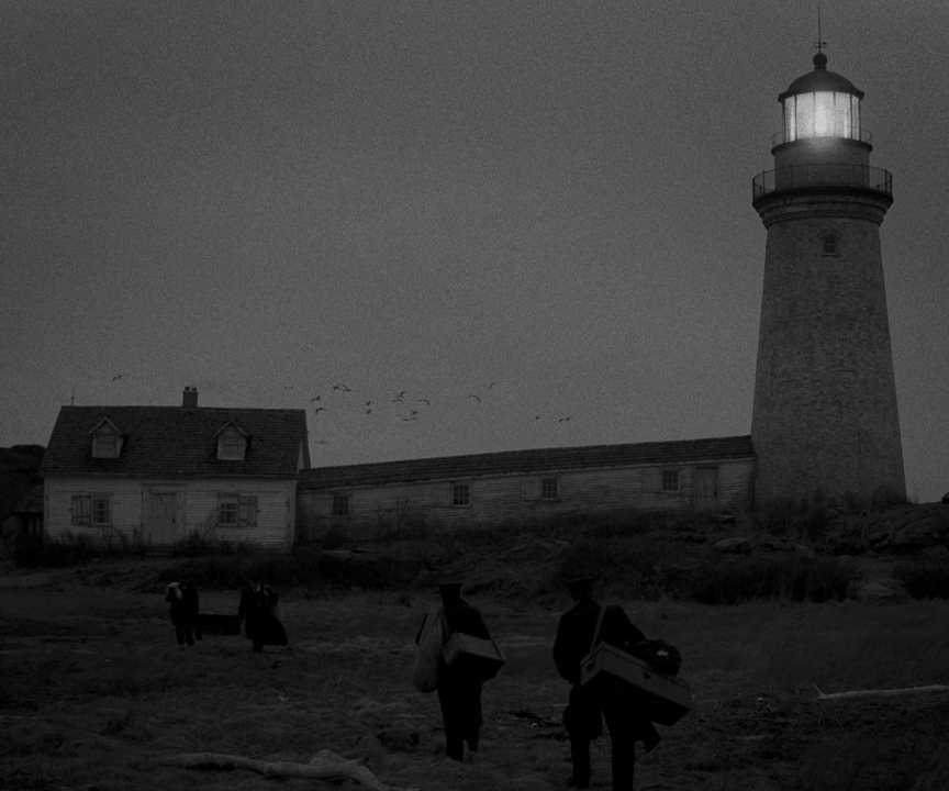 What Does a Cinematographer Do? Job Description & Real DP Examples 3 Four men walk toward a lighthouse and cottage in a dark, grainy black-and-white scene.