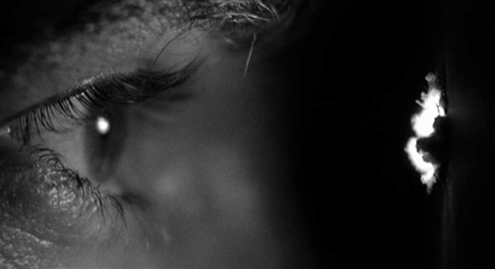 What Are the Stages of Dramatic Irony? Definition with 3 Film Examples 2 Close-up of an eye peering through a peephole in a dark room.