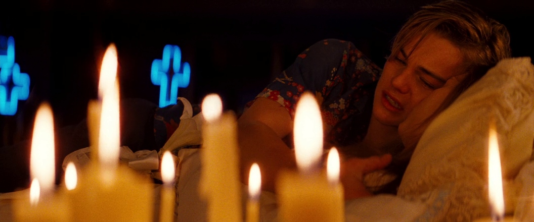 What Are the Stages of Dramatic Irony? Definition with 3 Film Examples 3 Romeo lies beside Juliet, surrounded by candles, with glowing blue crosses in the background.