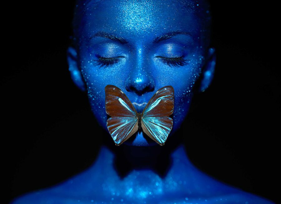 Types of Photography: Genres, Styles & Techniques Explained 39 Portrait of a woman with blue body paint lit with butterfly lighting, showing a soft shadow under the nose shaped like a butterfly against a dark background.