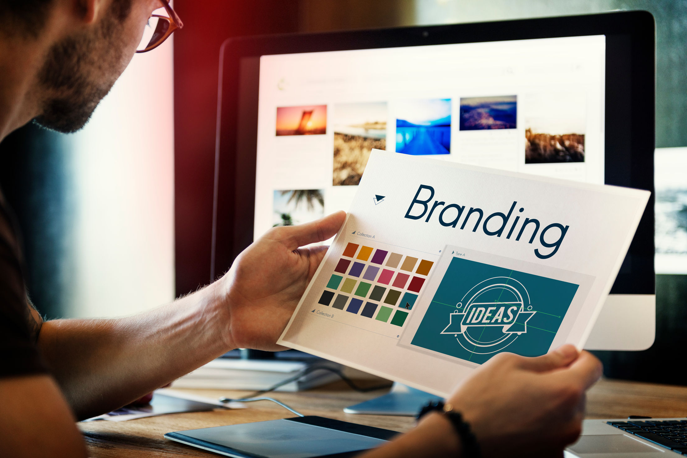 What Is Brand Photography? Definition, Uses & Planning Steps 5 A person holds a branding design sheet showing color palettes and a logo marked 'IDEAS'" title="Branding design sheet with color palettes and concept logo