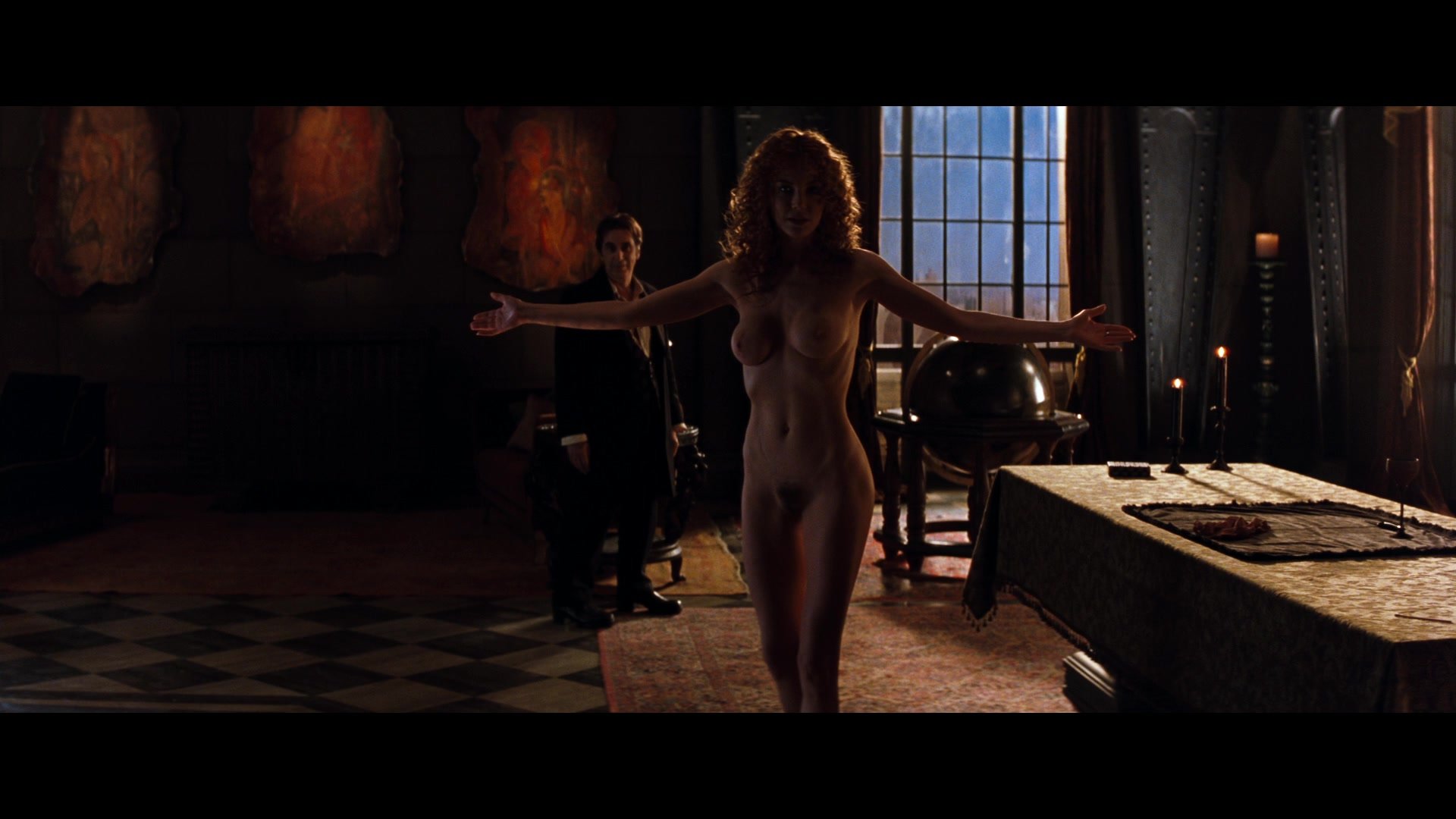 What Is a Deal with the Devil? The Trope Explained 2 Nude woman with arms outstretched in front of a man in a dark, ornate room. The scene represents temptation in The Devil’s Advocate.