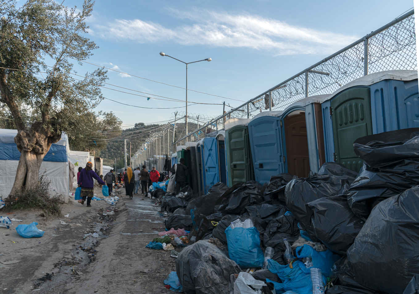 Types of Photography: Genres, Styles & Techniques Explained 7 People walking in a refugee camp with portable toilets and piles of trash bags