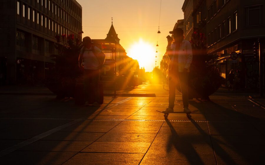 What Is Lens Flare? Types, Causes & Control 2 Golden hour street photo in Copenhagen with rim-lit silhouettes, long shadows, and warm sunlight flaring between buildings
