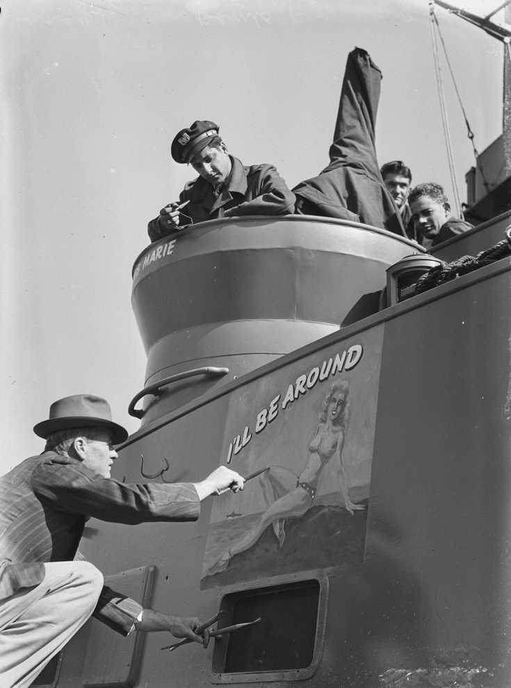 What Is Glamour Photography? Definition & Complete Guide to Style 4 WWII artist painting a blonde pin-up girl with “I'll Be Around” slogan on navy patrol boat