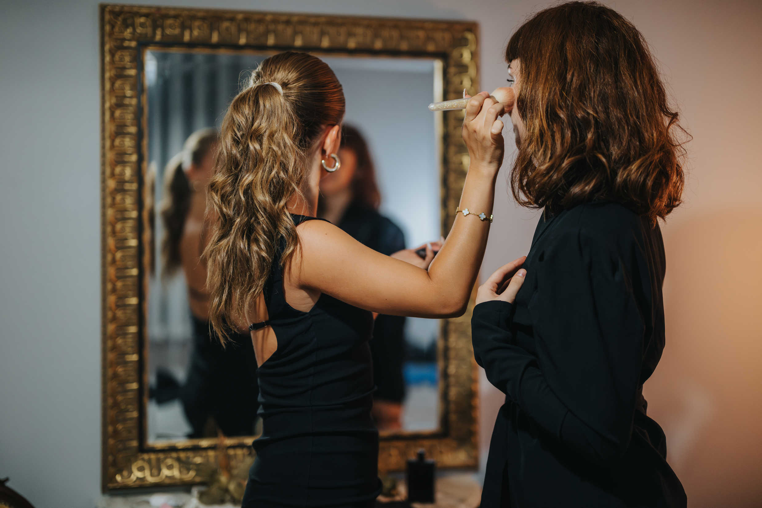 What Is Glamour Photography? Definition & Complete Guide to Style 15 A makeup artist applies blush to a woman’s face in front of a mirror before a glamour photoshoot.