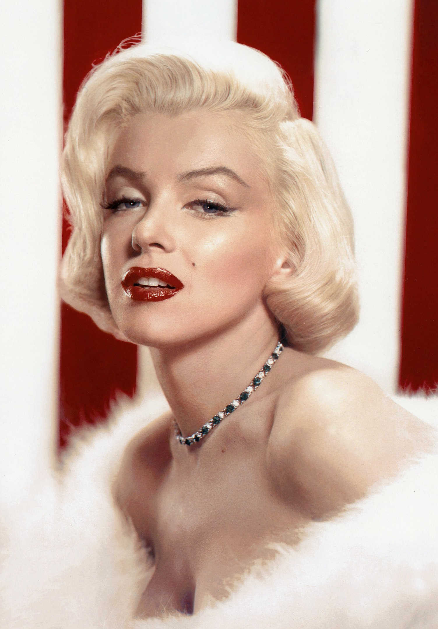 What Is Glamour Photography? Definition & Complete Guide to Style 5 Marilyn Monroe with red lipstick and styled platinum hair, posing in a fur wrap in front of a red-and-white striped background.