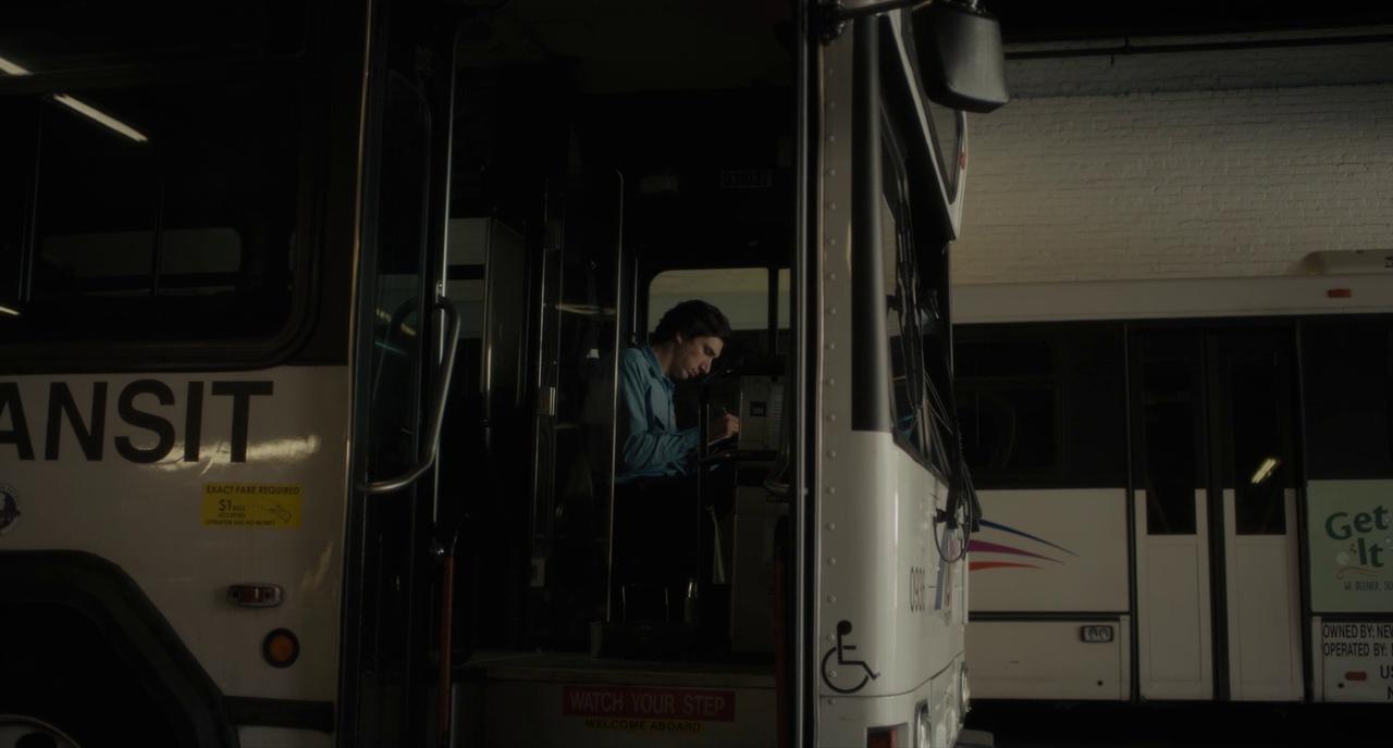 What Is Lyric Poetry? Definition & Examples Explained 2 A man sits in a bus driver’s seat in a dim depot and writes in a notebook; the bus doorway and other buses fill the background.