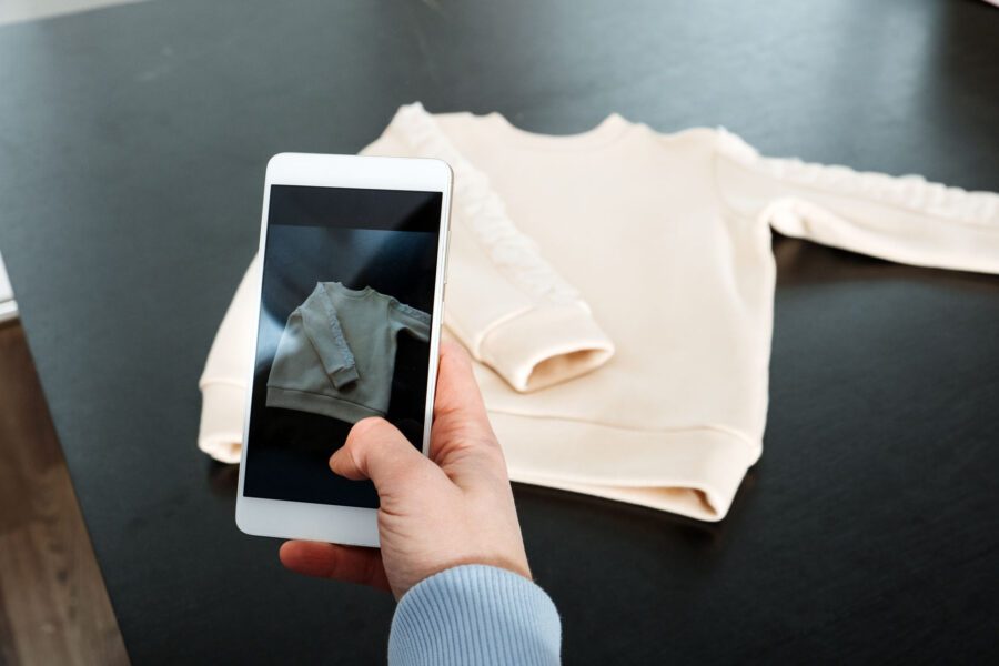 What Is Brand Photography? Definition, Uses & Planning Steps 6 A person takes a smartphone photo of a light-colored long-sleeve sweatshirt on a table