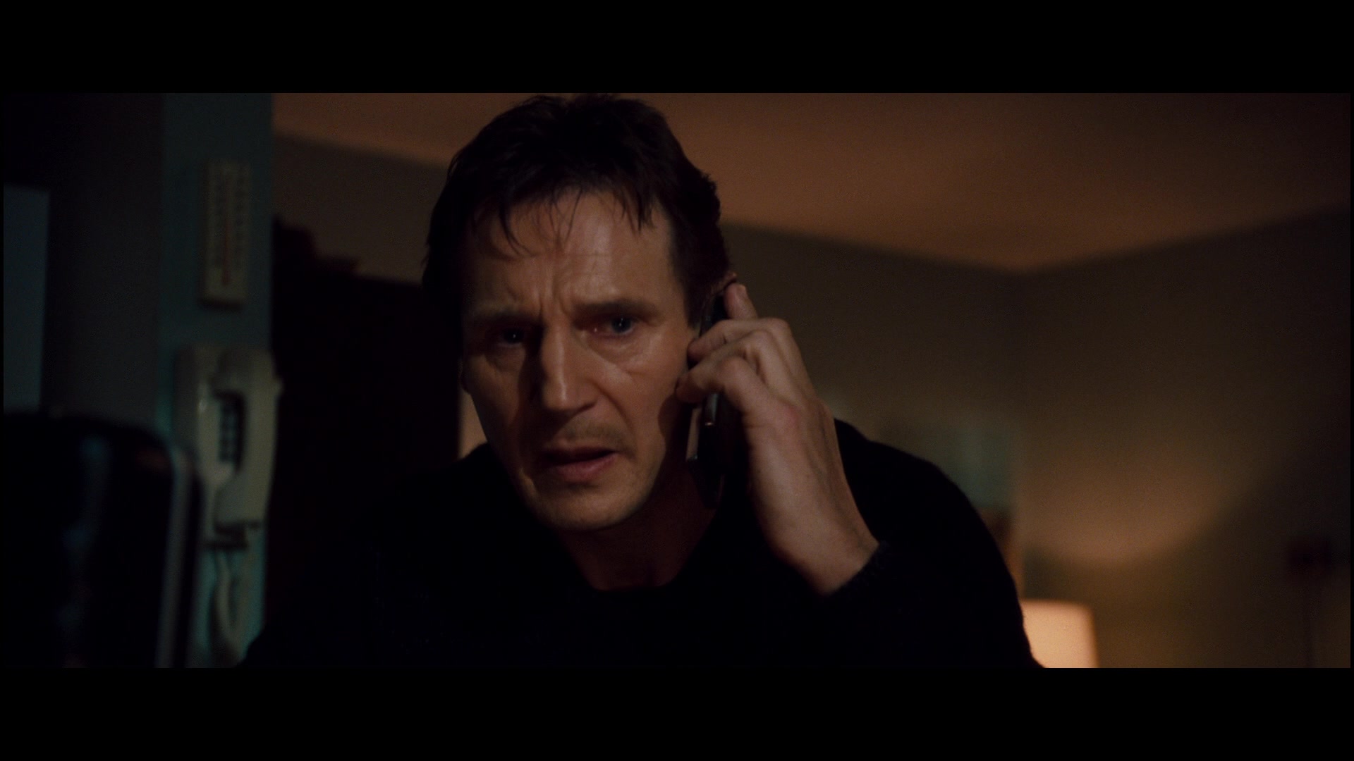 What Is an Overstatement? Definition & Examples from Film 5 A tense close-up of Bryan Mills holding a phone to his ear in a dimly lit room.