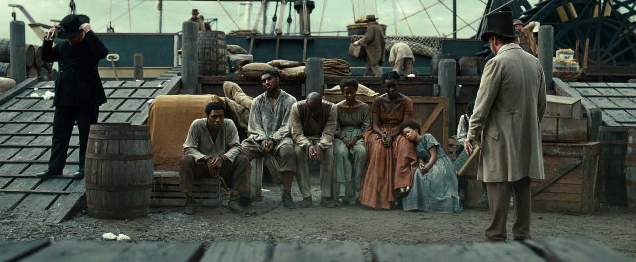 What is Empathy? Definition & Film Examples 3 A group of enslaved people sit in chains on a wooden dock while a man in a top hat observes them