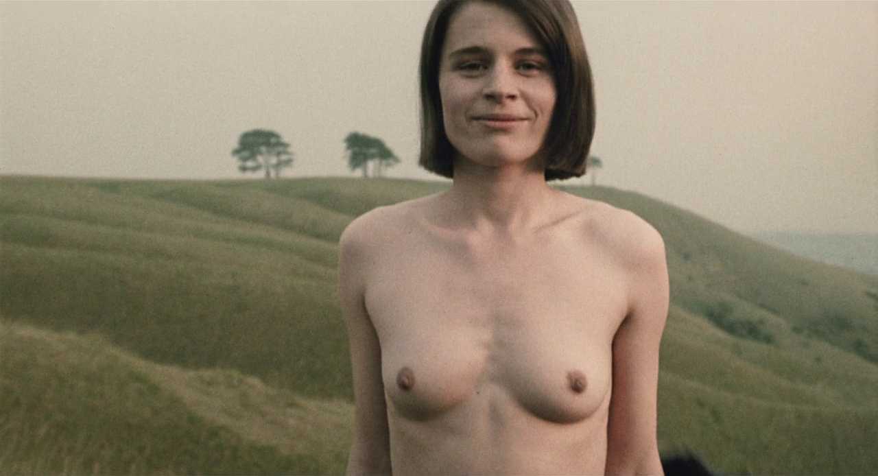 What Is Dystopian Fiction? Meaning + Examples from Film 3 A topless woman stands in a grassy field, facing the camera with a slight smile. Her presence represents defiance and sparks change in the male protagonist.