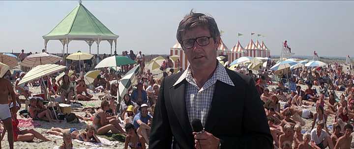 Rising Action in Film: Meaning, Function & Examples 7 A TV news reporter stands on a crowded beach with people sunbathing and swimming under umbrellas