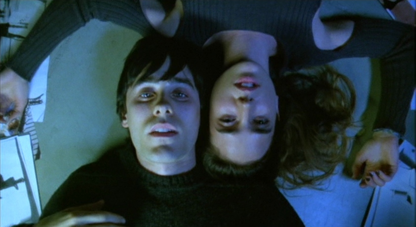 Requiem for a Dream overhead shot of two characters on the floor Two people lie on the floor with their heads close together, viewed from above under cool blue lighting.