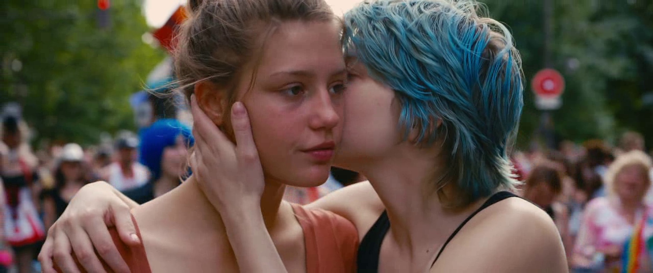 What Is Queer Theory? Definition & Film Examples 2 Emma with blue hair kisses Adèle on the cheek at a crowded pride parade.