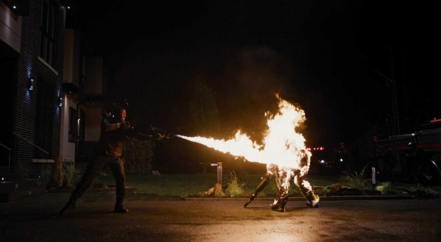 What Is Dystopian Fiction? Meaning + Examples from Film 5 A man in tactical gear uses a flamethrower to set another man on fire in front of a modern house at night.