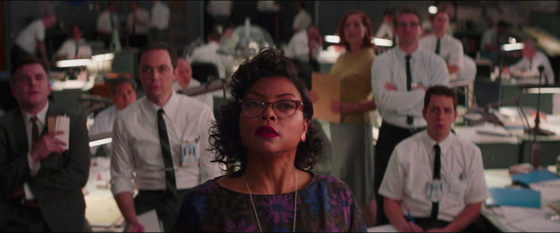 20 Movie Themes for Screenwriters to Explore 17 Katherine Johnson stands confidently in front of seated NASA staff in a large open office.