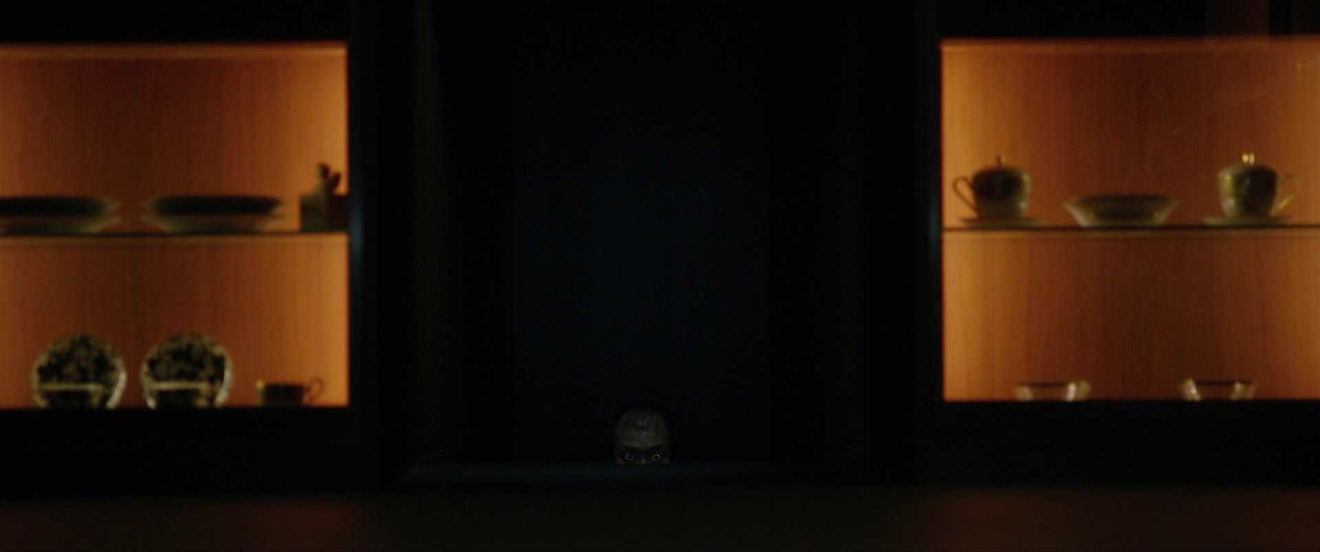 Kairos in Film, Ads & Speech: Why Timing Matters 4 A dimly lit room shows a man’s eyes and forehead barely visible from the shadows below a cabinet, surrounded by warm-lit dishes and tea sets.