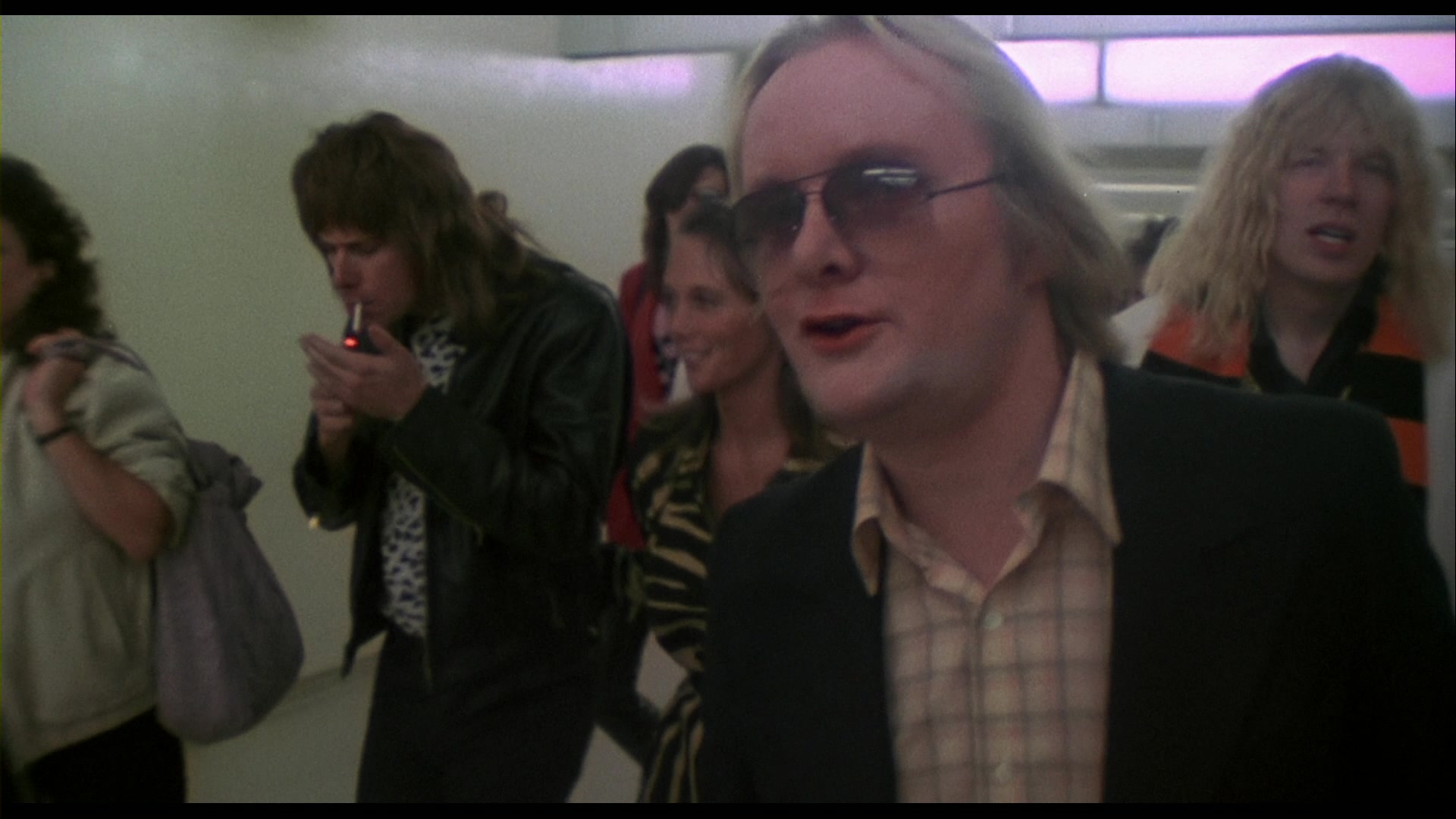 What Is a Talking Head Shot? Definition + How to Use It 5 David St. Hubbins walks in a hallway, addressing the camera in a medium close-up mockumentary shot, wearing sunglasses and a plaid shirt.