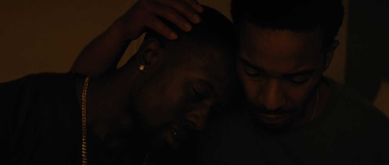 What Is Queer Theory? Definition & Film Examples 7 Two Black men sit closely with their heads leaning together in a dimly lit room, eyes downcast.