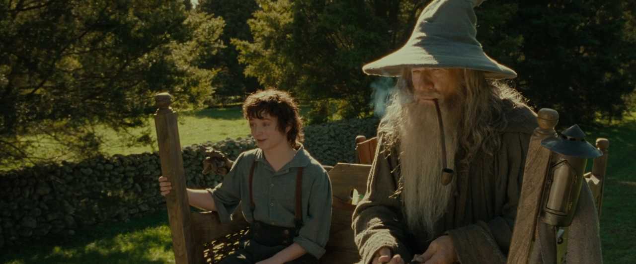 Forced Perspective in The Lord of the Rings Frodo and Gandalf ride on a wooden cart in a sunny field, with Gandalf appearing larger due to his closer position to the camera.