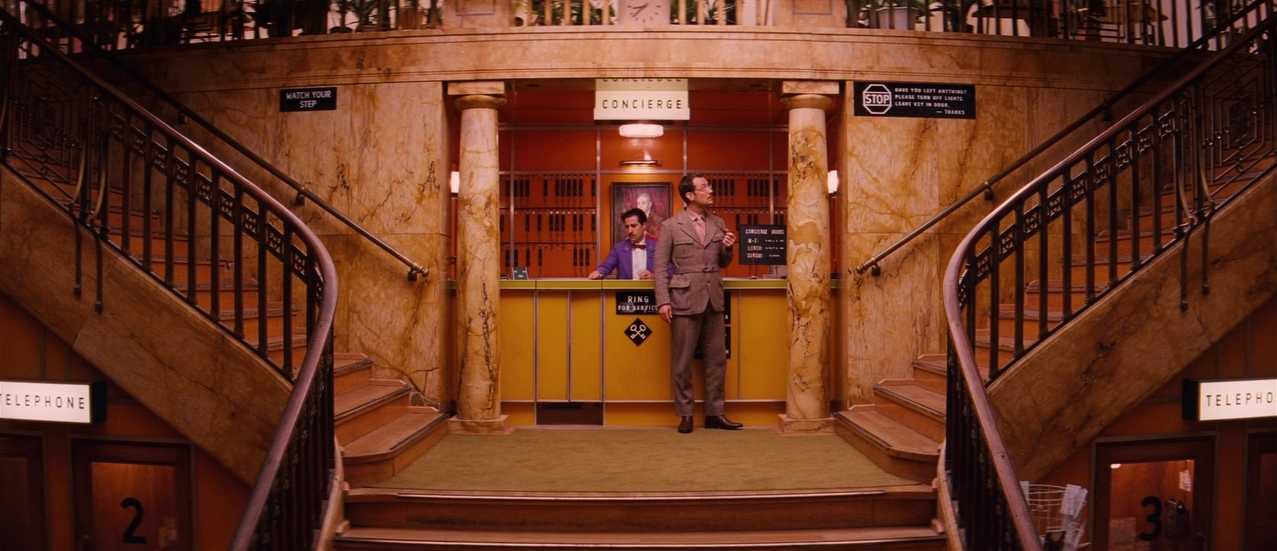 What Is a Focal Point in Art? Definition and Film Use 9 Two characters stand behind a concierge desk in a grand hotel lobby, framed symmetrically by two staircases.