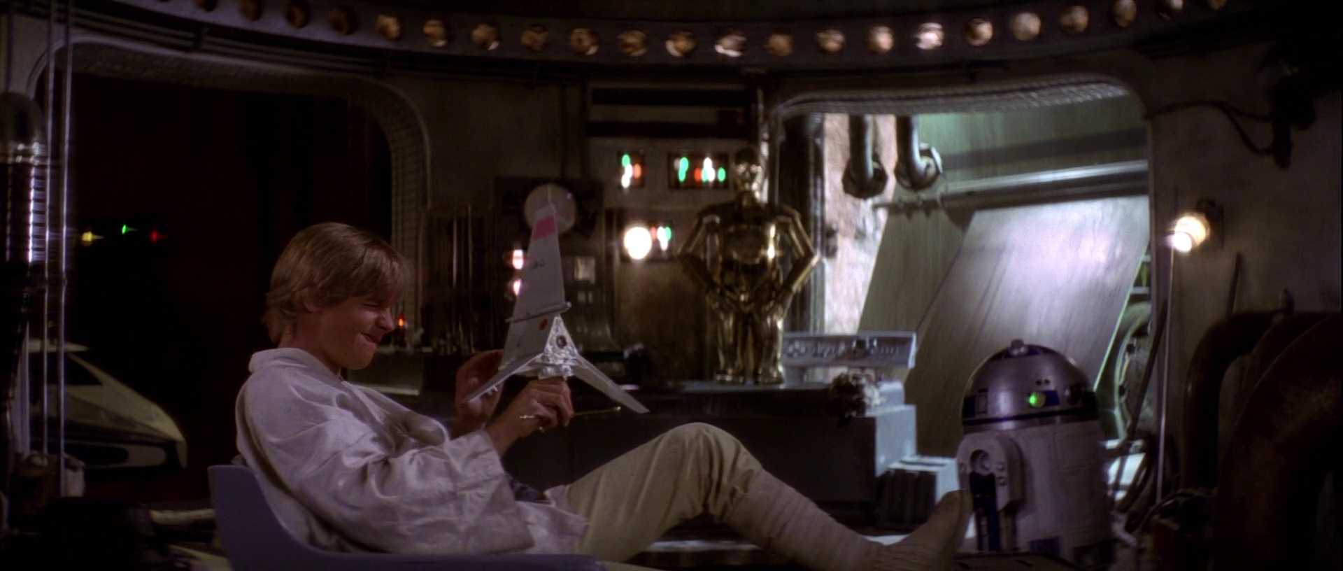 What is The Hero’s Journey? Story Structure Explained with Star Wars 2 Luke Skywalker leans back in a chair, smiling as he plays with a toy spaceship in his garage-like home on Tatooine. C-3PO and R2-D2 are nearby.