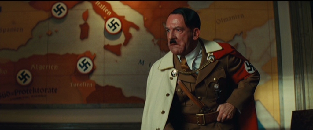 What Is World Building in Movies? Definition, Meaning & Examples 5 A man dressed as Hitler stands in front of a map of Europe covered in swastikas, angrily gesturing during a war meeting.