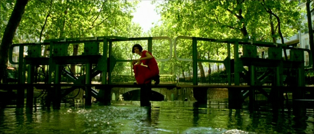 What Is a Complementary Color Scheme? (With Film Examples) 7 Amélie crouches on a green bridge in a red dress above reflective green water