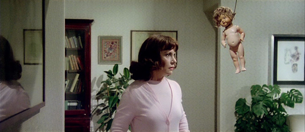 What Is Italian Exploitation Cinema? From Sex to Cannibalism 2 A woman in a pink sweater stares at a hanging doll suspended by a string in her apartment
