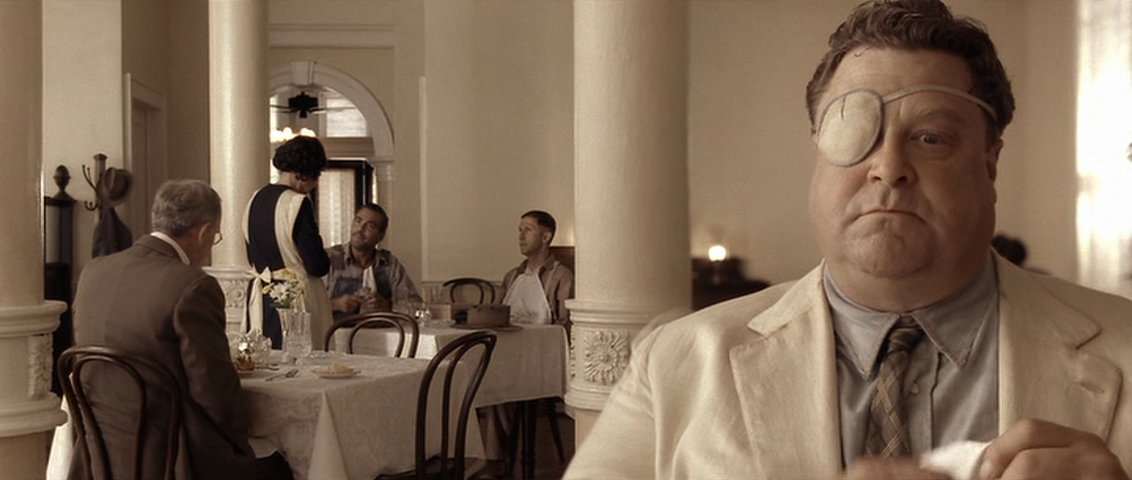 What Is a Color Palette? How to Use it in Film (+Free Planner) 11 A man with an eyepatch in a cream-colored suit sits at a restaurant table; the entire scene is washed in a warm, sepia tone