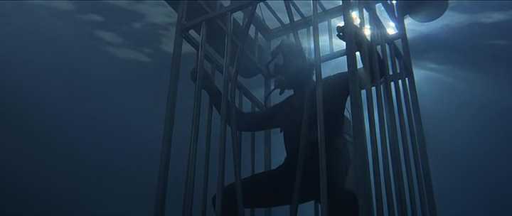 Atmosphere in Film: Definition, Meaning & Examples 8 Scuba diver stands inside a metal shark cage deep underwater with sunlight barely reaching through