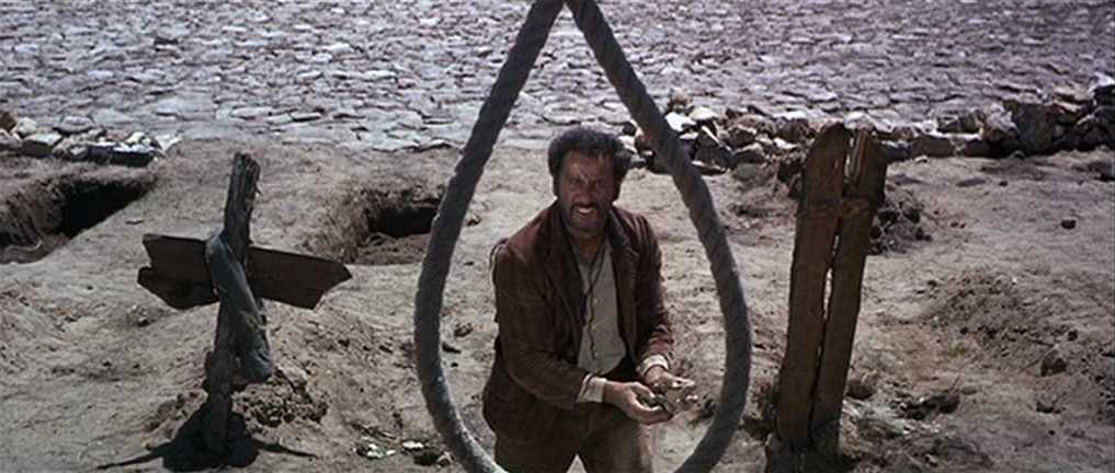What Is Italian Exploitation Cinema? From Sex to Cannibalism 3 A man stands under a noose in a barren graveyard with dry cracked earth and wooden crosses