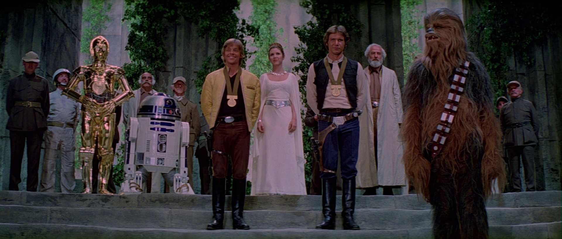 What is The Hero’s Journey? Story Structure Explained with Star Wars 9 Luke Skywalker and Han Solo stand proudly with medals, flanked by Leia, Chewbacca, C-3PO, R2-D2, and Rebel soldiers during a victory ceremony on Yavin 4.