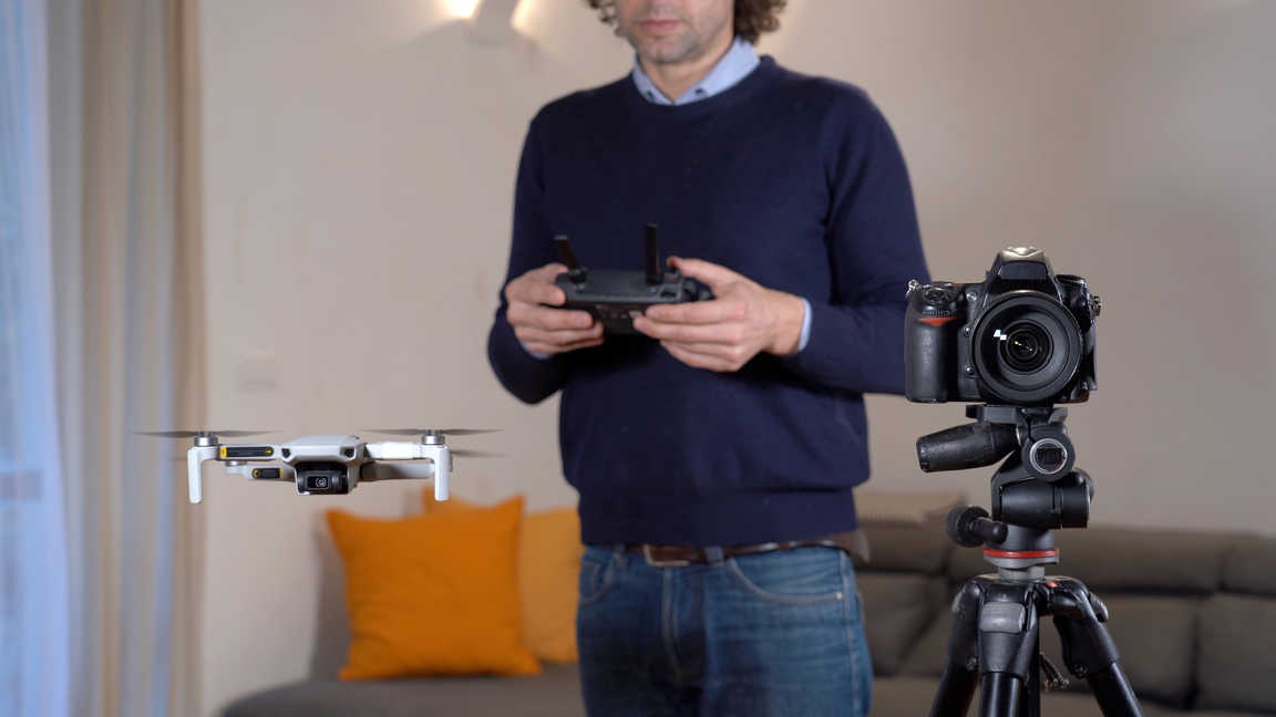 What Is Commercial Photography? Definition and Uses 3 Photographer flying a drone indoors while DSLR camera is set up on a tripod for real estate shoot