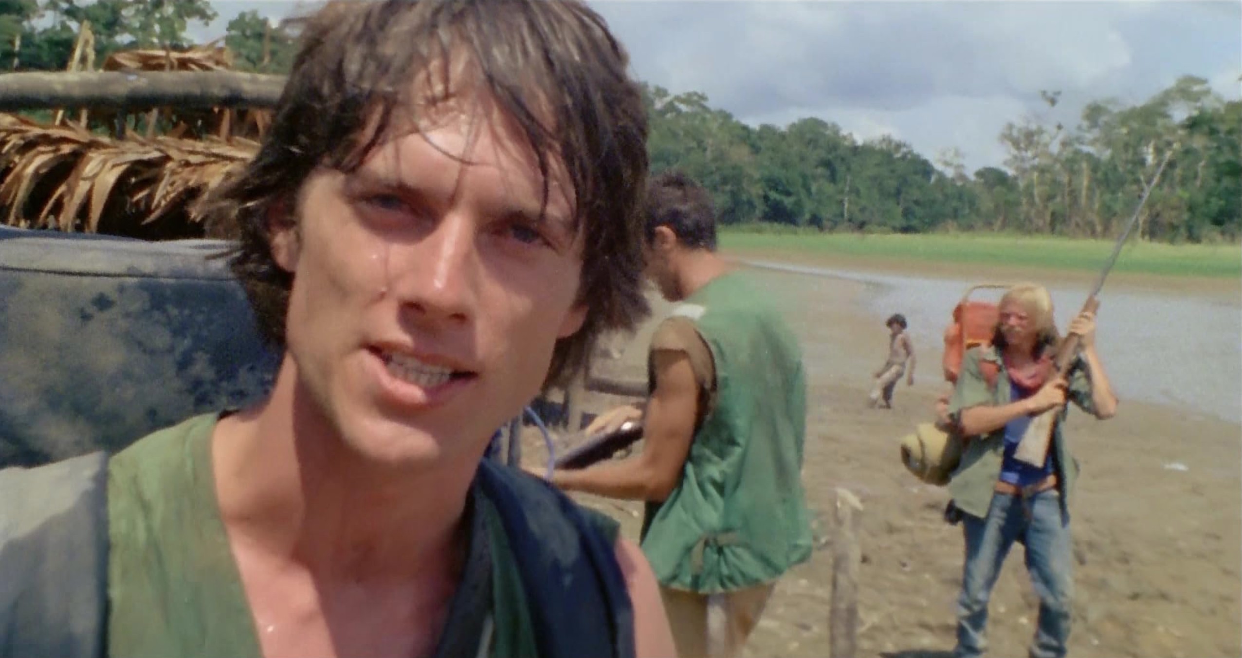 What Is Italian Exploitation Cinema? From Sex to Cannibalism 5 A sweaty man looks into the camera while two other men with rifles stand behind him on a muddy riverbank
