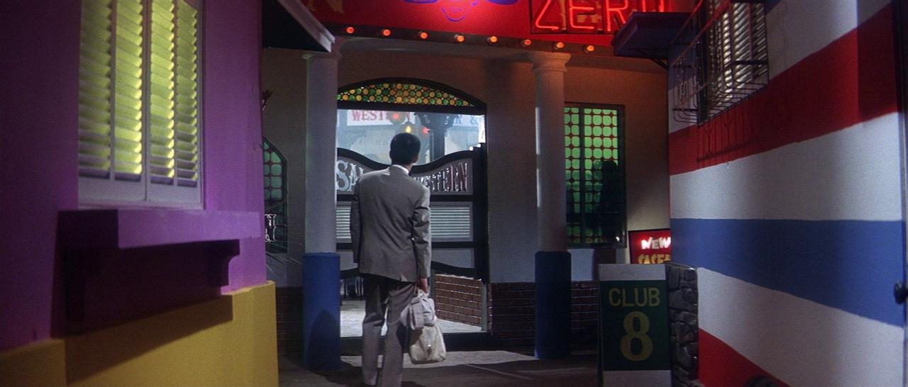 What Is an Analogous Color Scheme? Definition & Film Examples 2 A man in a suit approaches a neon-lit club entrance surrounded by violet, blue, and red walls.