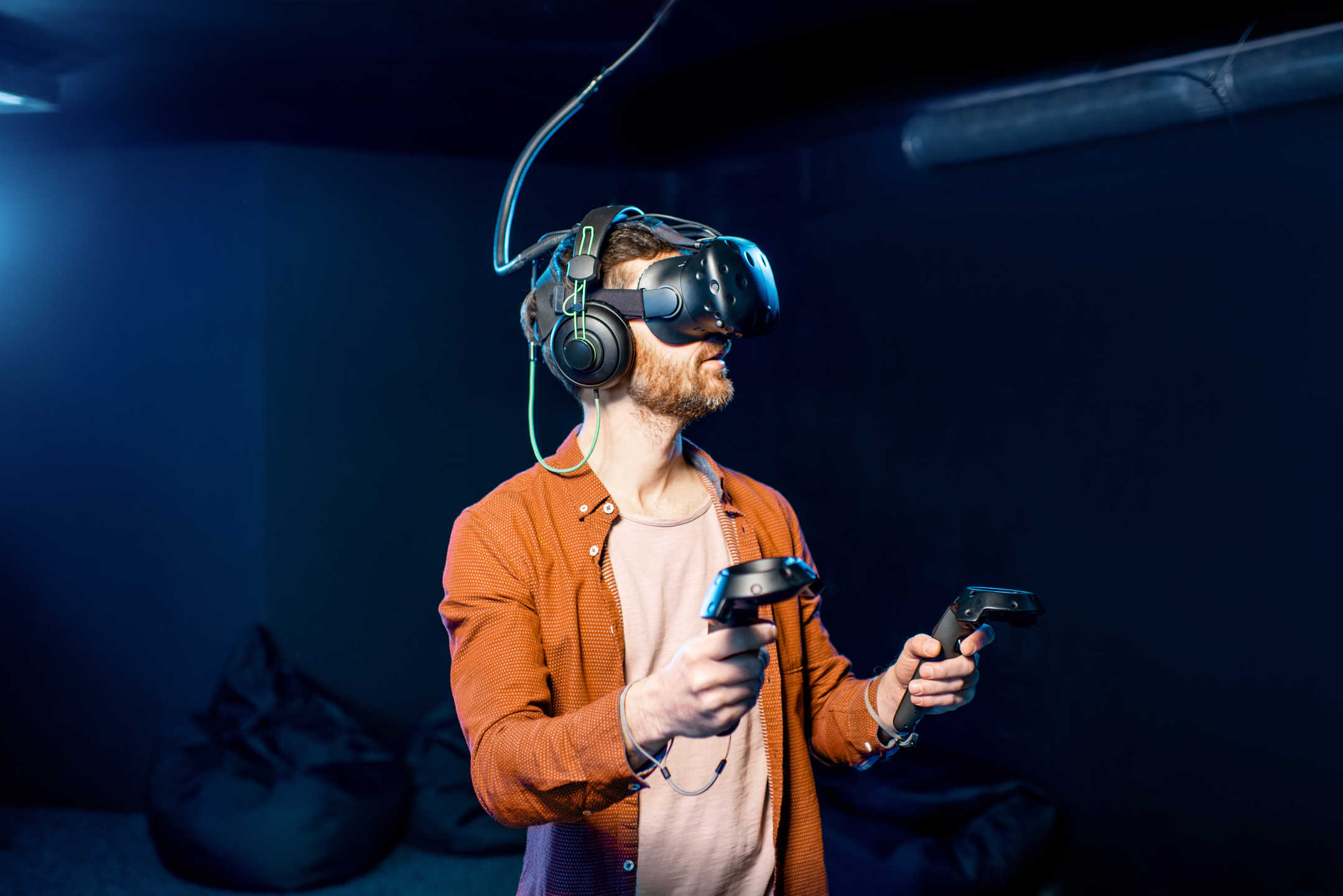 What Is Virtual Reality? Definition, Film Uses & Future Trends 3 Bearded man using VR headset with hand controllers in dark room