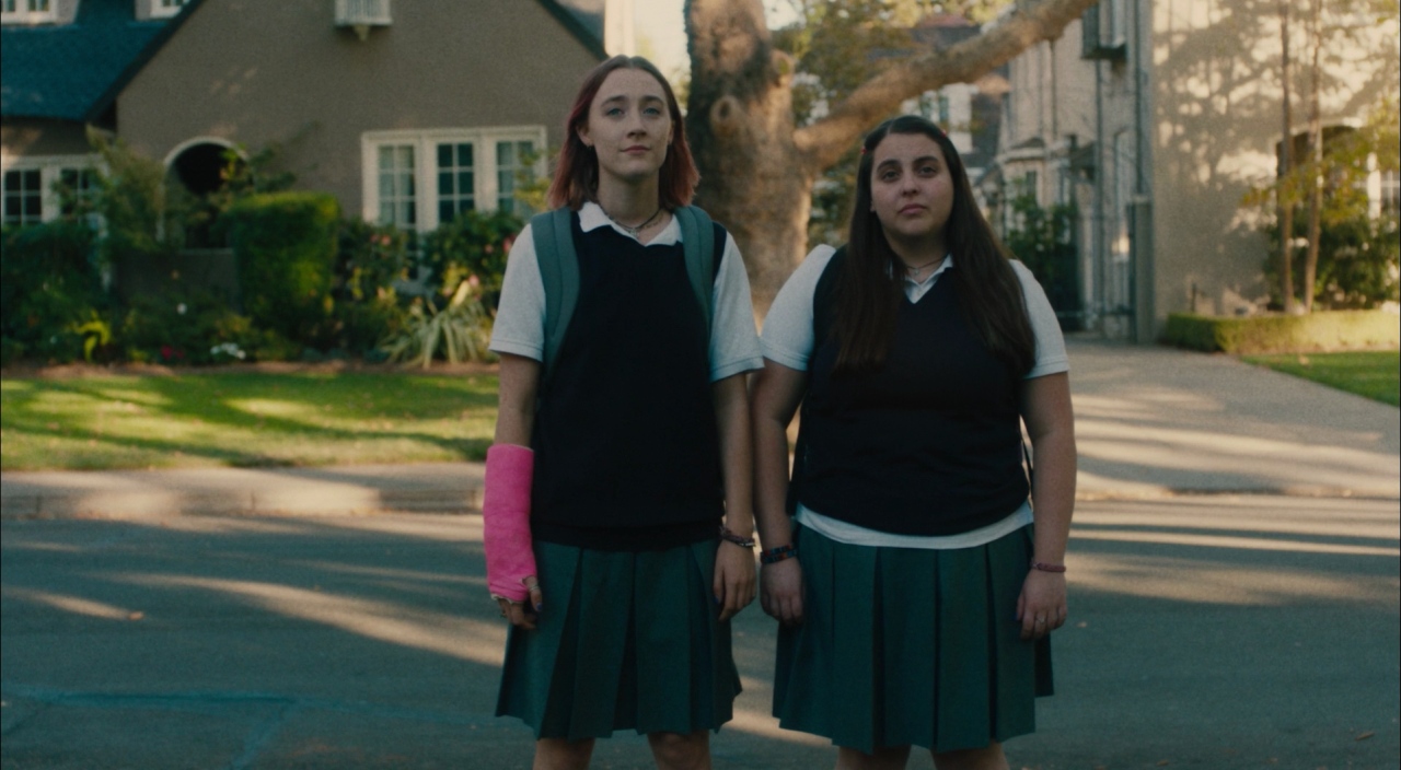 What Is World Building in Movies? Definition, Meaning & Examples 6 Two teenage girls in school uniforms stand side by side on a suburban street, with one wearing a bright pink arm cast.