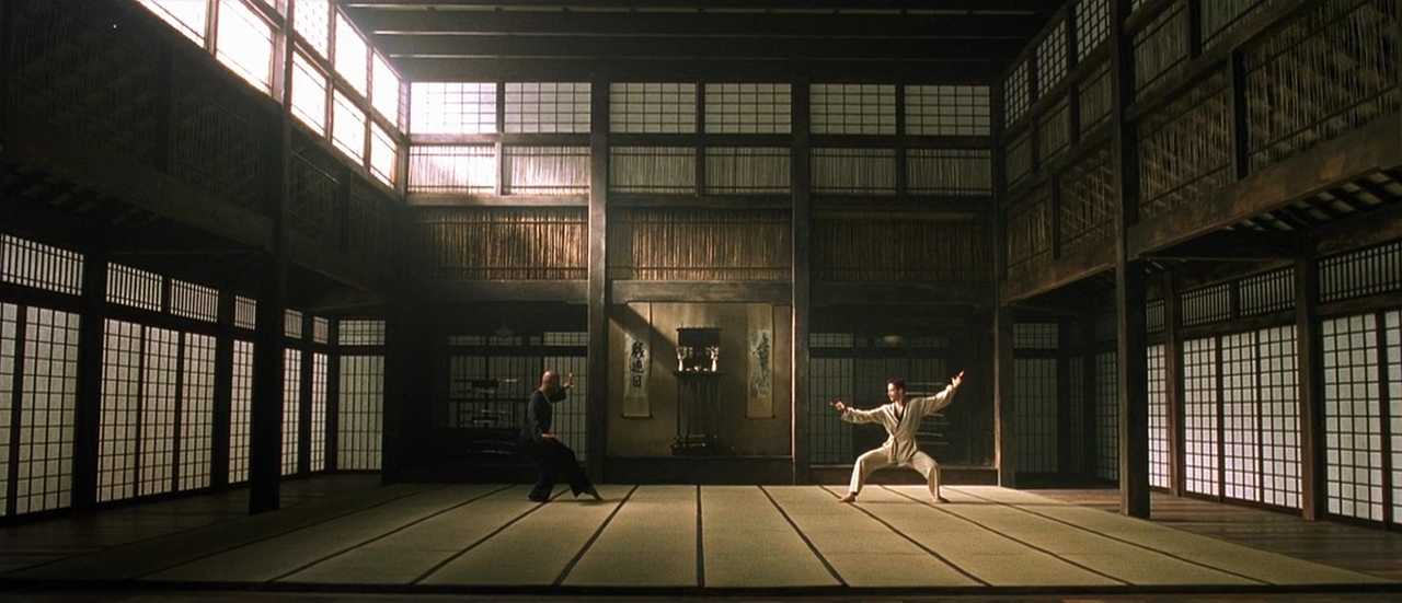 What Is World Building in Movies? Definition, Meaning & Examples 8 Two men face each other in fighting stances inside a traditional Japanese-style dojo filled with soft light and wooden architecture.