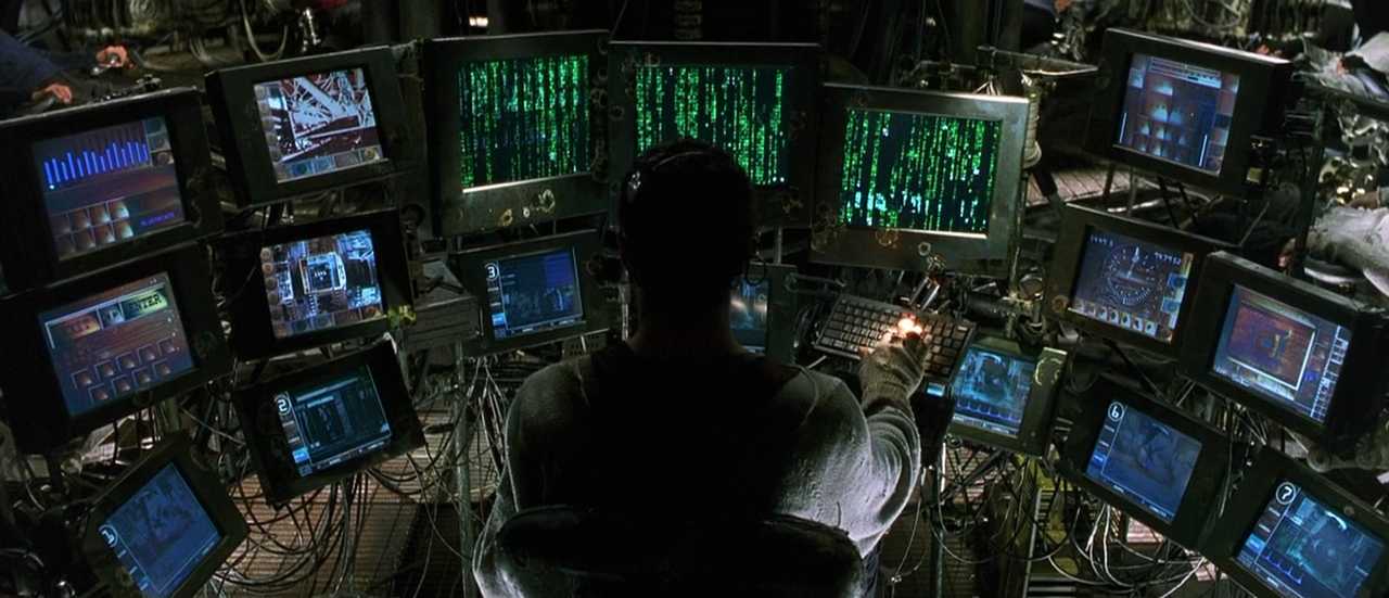 What Is a Color Palette? How to Use it in Film (+Free Planner) 9 A man sits surrounded by dozens of glowing monitors displaying green code and system graphics.