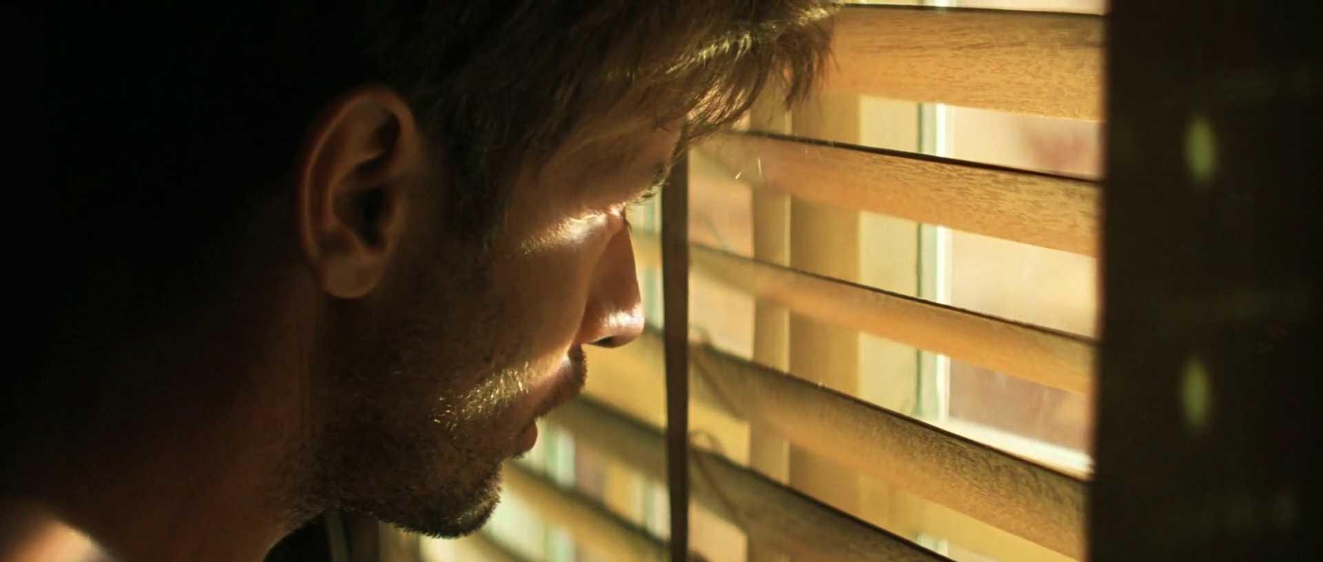 What Is Motivated Lighting? Definition, Why, and How It’s Used on Set 4 Side-profile close-up of Captain Willard looking through horizontal window blinds, with warm bands of light across his face and the room falling into shadow.