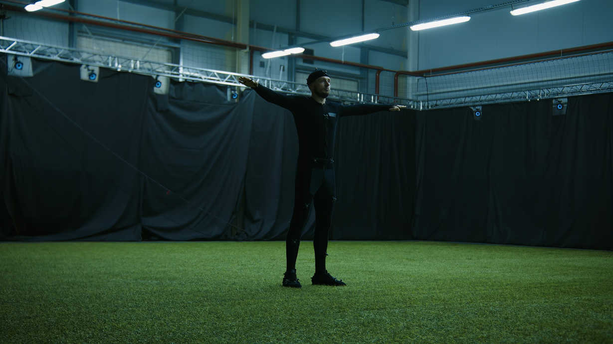 Post-Production in Film: Definition, Steps & Roles 6 A performer in a motion-capture suit stands in a T-pose inside a studio with tracking cameras for calibration before animation.