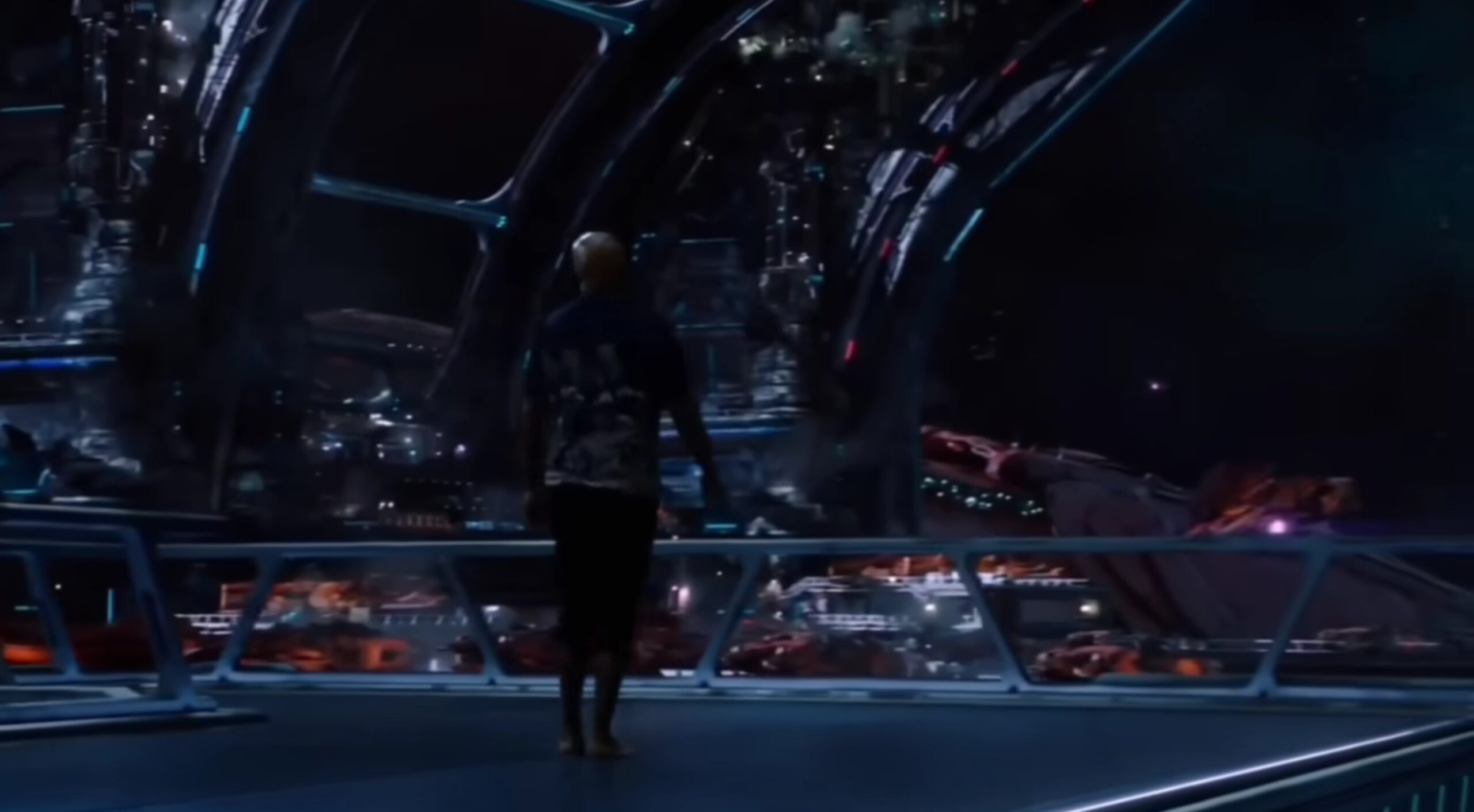 What is an End-credit Scene? Definition, Uses, and Film Examples 3 A bald man stands inside a futuristic space station corridor with curved beams and windows, looking out at a vast sci-fi structure filled with lights and spacecraft.