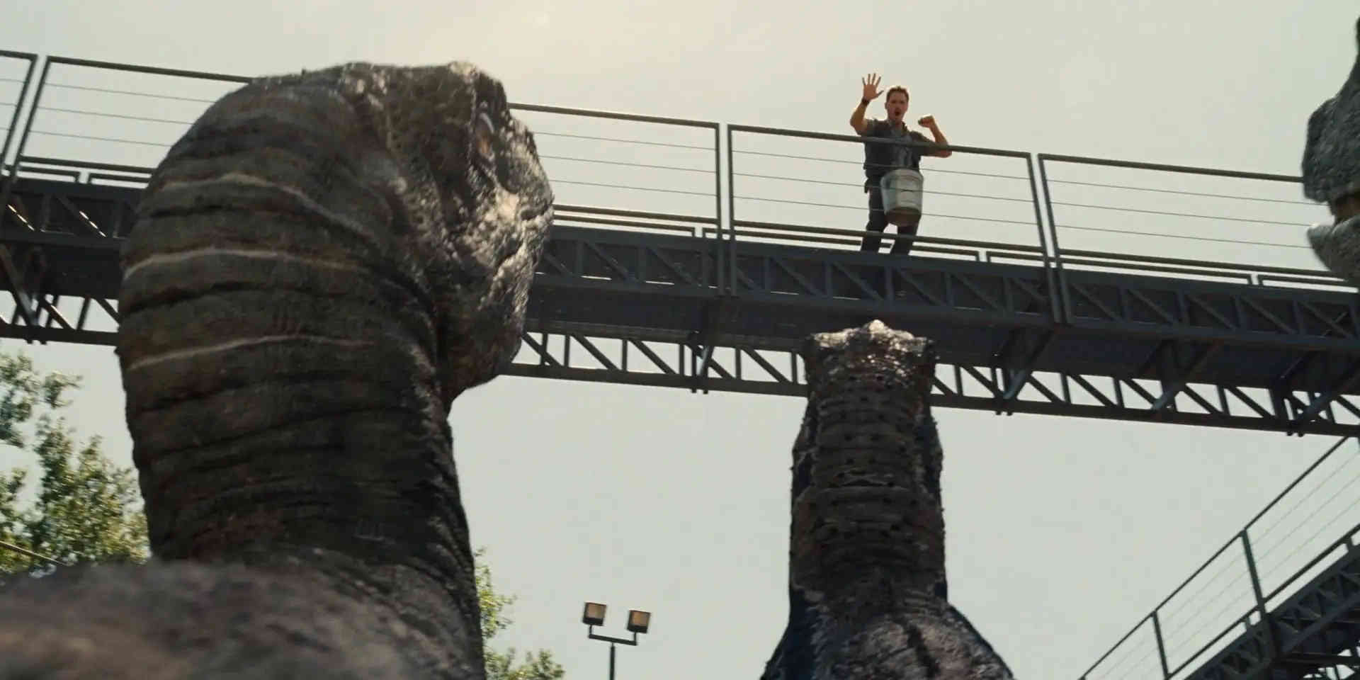 What is a 2:1 Aspect Ratio? Definition, Workflow & Film Examples 4 A low-angle shot of a raised metal walkway with a boy standing near the railing, one hand lifted. Two massive dinosaur bodies rise into the foreground from below, framing the bridge against a pale sky.