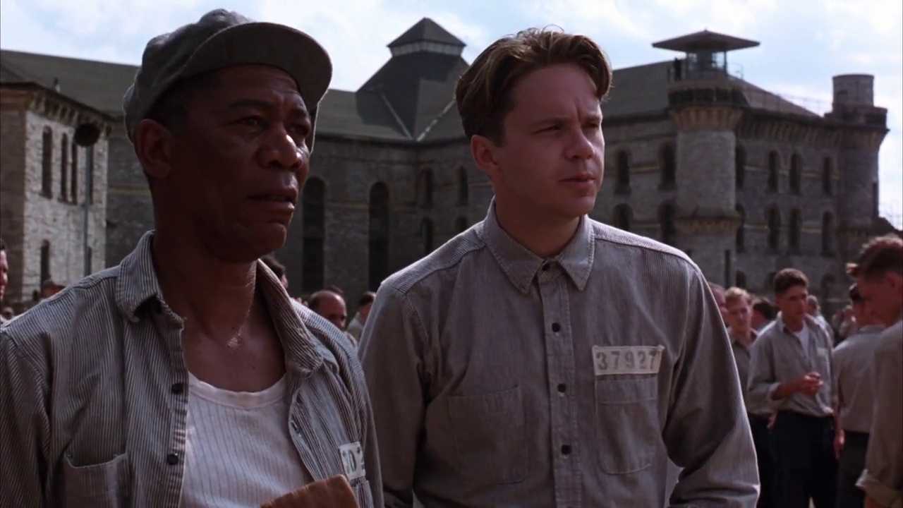 What Is a Protagonist? Definition, Role, and Function in Film 4 Red and Andy stand among other inmates in the Shawshank prison yard, with the prison buildings visible behind them.