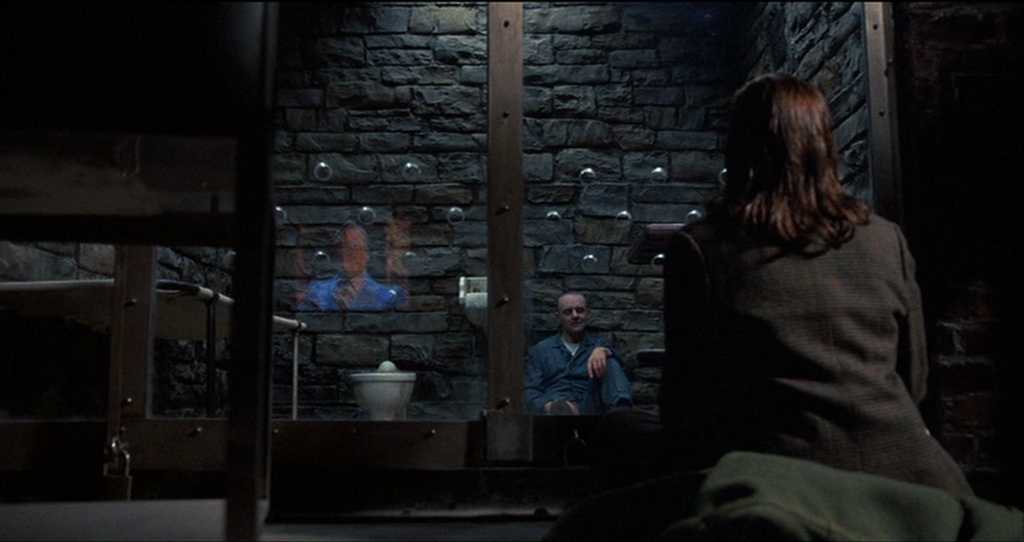 What is a Mystery Movie? Definition, Key Traits and Examples 4 Clarice Starling sits facing Hannibal Lecter behind glass in his stone cell, with Lecter seated calmly as they speak during an interrogation.