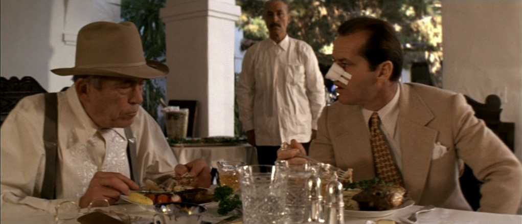 What is a Mystery Movie? Definition, Key Traits and Examples 2 Jake Gittes and Noah Cross sit at a lunch table mid-conversation, with Cross calmly eating as Gittes listens, suggesting hidden information and control.
